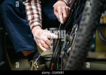 Male mechanic working in bicycle repair shop, mechanic repairing bike using special tool, wearing protective gloves. Young attra Stock Photo