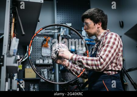 Young caucasian repairman repairing mountain bike wheel in bike shop workshop. Fixing bicycle. Caring for you wheels. man mechan Stock Photo