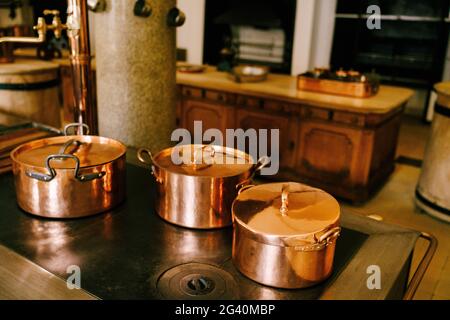 Three copper pots on the stove against the background of a long wooden table in a vintage dining room. Stock Photo