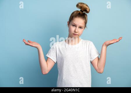 Confused girl teen with open arms on a blue background. Isolated on blue background, copy space, place for advertising. Stock Photo