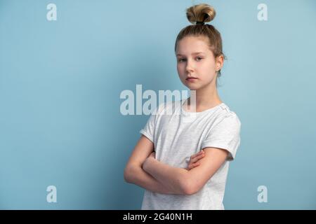 Girl with blond hair on a blue background. Beautiful girl folded her arms across her chest. Stock Photo