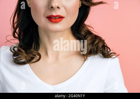 On a pink background, half of a woman's face, red lips. Portrait of a woman for advertising, copy space, place for text, blank wall. Stock Photo