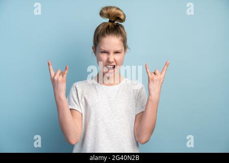 Happiness little girl showing rock and roll sign. Indoor, studio shot on blue background Stock Photo