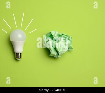 Crumpled colored balls of paper and glass white lamp on green background Stock Photo