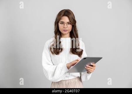 Beautiful girl with glasses working on a tablet, she is seriously looking at the camera. Brunette isolated on gray background., Beautiful girl with gl Stock Photo