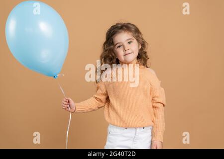 Very cute, attractive, little girl with a balloon on a brown background. Smiling girl posing on the background of an empty wall, Very cute, attractive Stock Photo