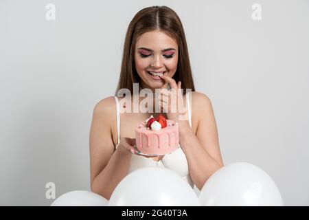 Sweet, attractive, well-groomed girl holds an appetizing cake, looks at it sincerely, wants to eat it. Beautiful, young woman on a white background, S Stock Photo