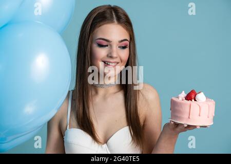 Charming brunette bit her lip, really wants to eat a cake in her hand. Cute girl posing on a blue background, Charming brunette bit her lip, really wa Stock Photo
