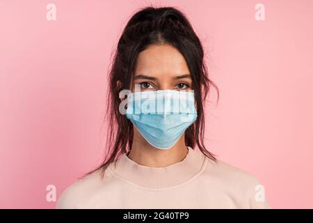 Attractive young brunette wears a protective mask isolated on a pink background. Cute, beautiful girl isolated on a pink background, close-up view Stock Photo