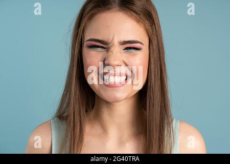 Close-up, the girl is smiling broadly with her teeth, she closed her eyes. Cute girl on a blue background, Close-up, the girl is smiling broadly with Stock Photo