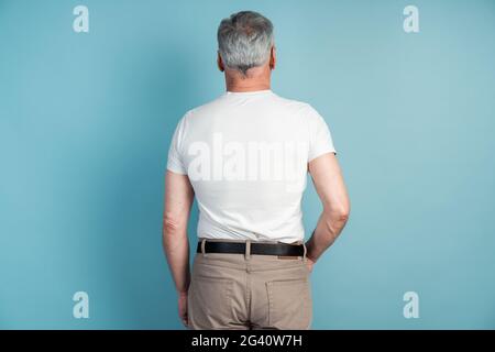 Rear view, a man in a white T-shirt with his back to the camera. Senior man isolated on blue background, copy space, place for text, Rear view, a man Stock Photo