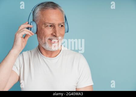 Attractive, smiling man in headphones posing on a blue background. The man looks to the side, copy space, place for advertising, Attractive, smiling m Stock Photo