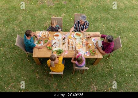 Overhead view of caucasian three generation family at table eating meal in garden making a toast