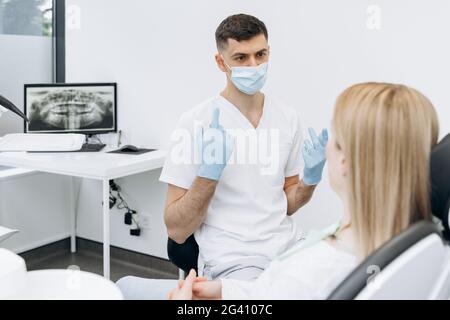 Attractive dentist in a protective mask communicates with an attractive patient. The dentist works in the dental office Stock Photo