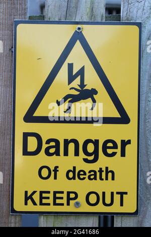 Danger of death keep out sign in yellow with black text and silhouette of man being electrocuted Stock Photo