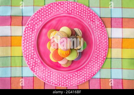 Macarons tower on pink dessert plate top view. Retro pink vintage tablecloth Easter table home kitchen. Assortment of pastel color macaron of Stock Photo
