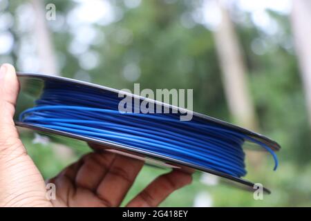 Spool of blue color wire called as 3D Printer filament held in hand on nature background Stock Photo