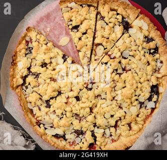 Baked round crumble pie with plum cut into pieces on a black background Stock Photo