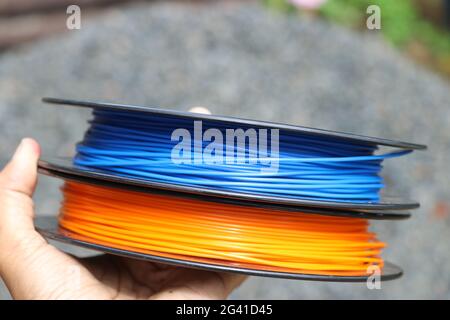 3D printing filament spools on hand. Blue and orange 3D Printer filaments for additive manufacturing Stock Photo