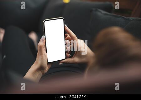 Girl using smartphone blank screen frameless modern design while lying on the sofa in garden Stock Photo