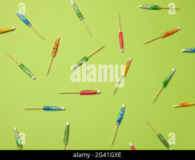 Colorful wooden cocktail umbrellas folded on a green background Stock Photo