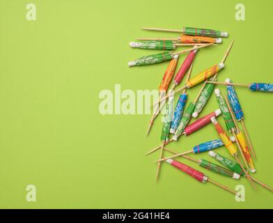 Colorful wooden cocktail umbrellas folded on a green background Stock Photo