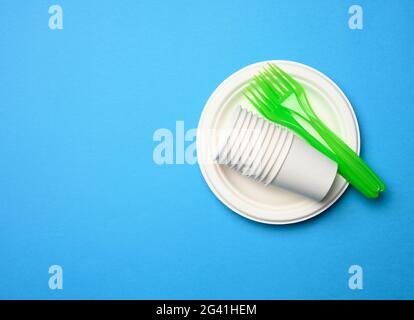 Green plastic forks and empty white paper disposable plates on a blue background, Stock Photo