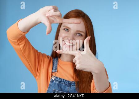 Joyful attractive sincere redhead young girl searching inspiration find perfect angle take good shot make hand frames look throu Stock Photo