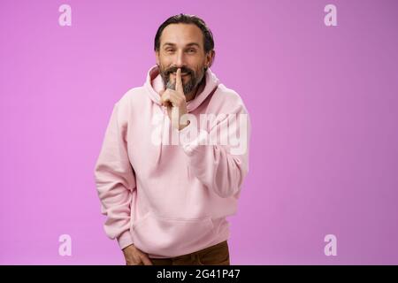 Lips sealed secret. Portrait alluring cheeky stylish adult bearded guy in pink hoodie asking keep quiet show shush shh gesture i Stock Photo