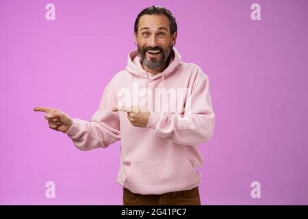 Charismatic happy good-looking mature 50s man wearing stylish hipster hoodie smiling excited pointing left index fingers impress Stock Photo