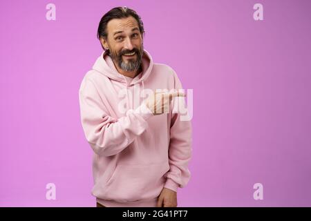 Friendly carefree caucasian bearded man in pink hoodie pointing right intoducing family members smiling proudly delighted showin Stock Photo