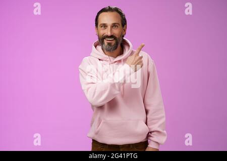 Good-looking lucky energized happy mature 50s man grey hair in trendy hipster hoodie pointing upper right corner amused telling Stock Photo