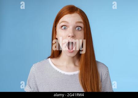 Wow so cool. Impressed speechless amused attractive redhead girl blue eyes freckles open mouth wide omg drop jaw astonished expr Stock Photo