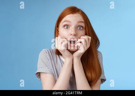 Shocked speechless gasping young redhead girl staring impressed stunned watching important moment tv series biting fingers open Stock Photo