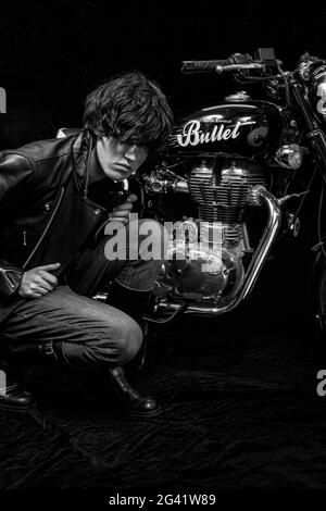 Young biker in black leather jacket with classic style motorcycle and black backround.Male biker indoor with cafe racer.
