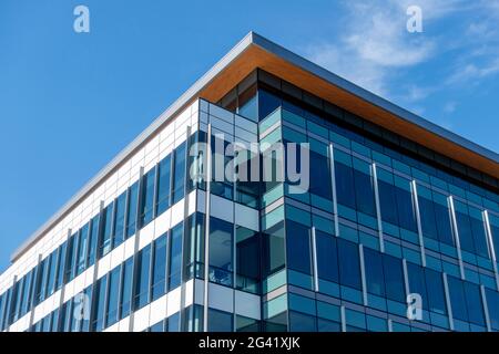 Angled view of a large, window covered building corner against a blue, cloud filled sky Stock Photo
