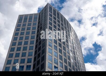 Angled view of a large, window covered building corner against a blue, cloud filled sky Stock Photo