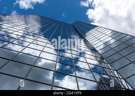 Angled view of a large, window covered building corner against a blue, cloud filled sky Stock Photo