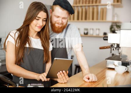 Coffee Business Concept - Satisfied and smile owners couple look on tablet orders online in modern coffee shop Stock Photo