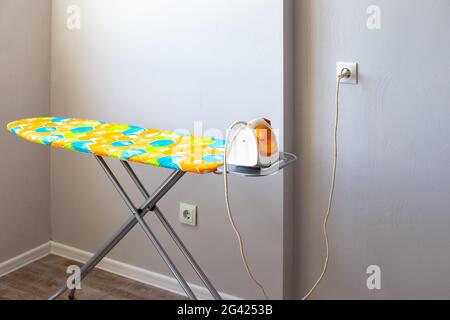 The electric iron on the ironing board is plugged into the socket. Safe ironing, smart home. Stock Photo