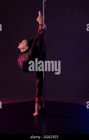 Graceful girl doing gymnastic exercise near pole in darkness Stock Photo