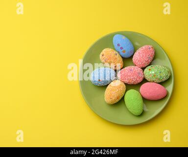 Decorative easter eggs in a round green ceramic plate on a yellow background, top view, Stock Photo