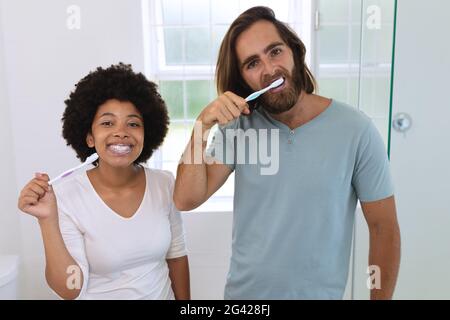 Portrait of happy diverse couple standing in bathroom brushing teeth Stock Photo
