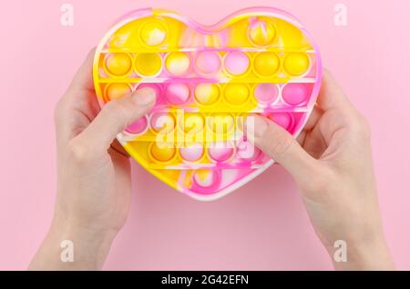 Pop it in the shape of a heart on a pink background. Children's modern toy pop it fidget in female hands. Silicone toy for the development of fine mot Stock Photo