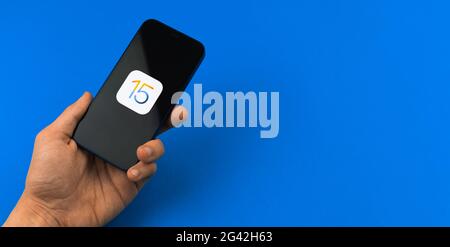 Kharkov, Ukraine - June 18, 2021: Man use mobile phone with newest software update, operating system iOS 15 on Apple iPhone, banner, blue background, Stock Photo
