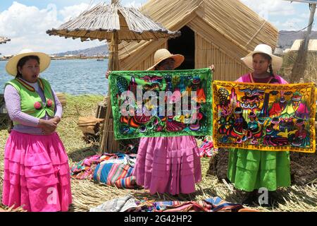 Selling art work at Lake and straw houses Lake Titicaca Peru cloth clothes colour pretty girls female females Peruvian women reed huts hut Island Stock Photo