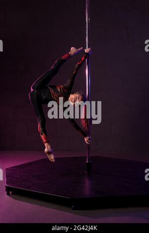 Graceful teem girl doing gymnastic split on pole in darkness Stock Photo