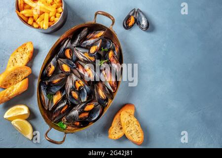 Mussels, shot from the top on a blue background with fries, toasts, and lemon Stock Photo