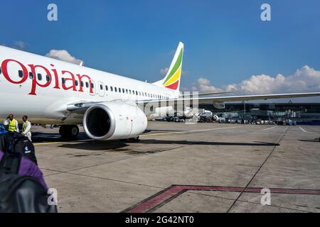 Addis Ababa, Ethiopia - April 23, 2019:  Ethiopian airlines Boeing 737 waiting at ground on sunny day, Bole International airport building in backgrou