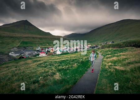 Woman walks on path in front of the village of Gjogv on Eysteroy, Faroe Islands Stock Photo